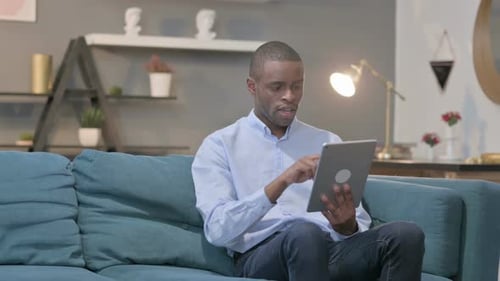 Young Man Using Tablet Sitting on Couch Indoors