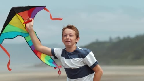 Boy running with kite at beach, slow motion