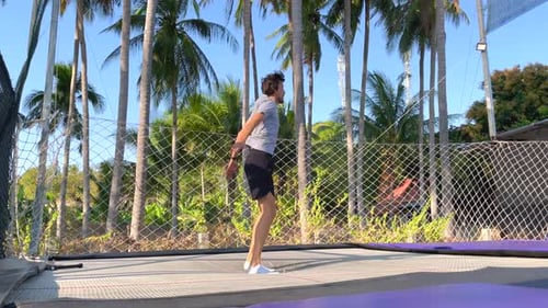 Man Exercising on a Trampoline Surrounded by Tropical Trees