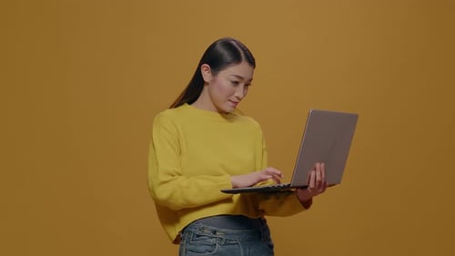 Woman Uses Laptop in Front of Yellow Background