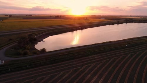 Sunset aerial view flying backwards over pond and farm field