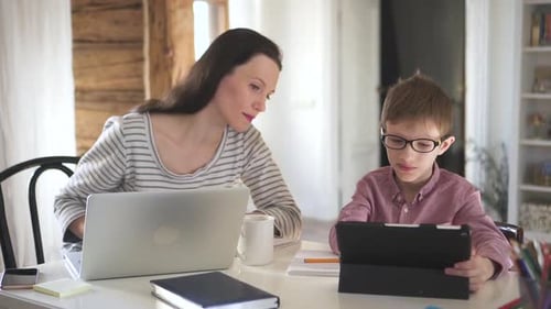 European Woman is Helping Son Who Learning Online with Tablet at Table in Apartment Room Spbd