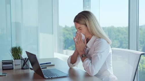Businesswoman Blowing Nose at Office Desk