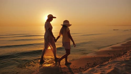 A Woman and Her Daughter Walk Together Along the Sand on the Beach
