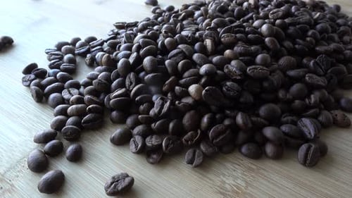 Pouring Dark Roast Coffee Beans onto Wooden Surface