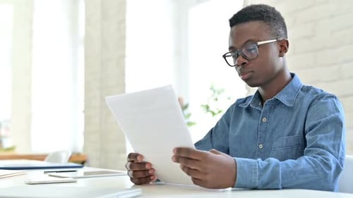 Focused Young African Man Reading Documents in Office