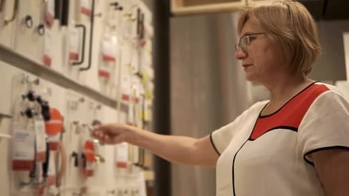 Elderly Woman is Examining Accessories for Furniture Fixed on a Stand in Shop
