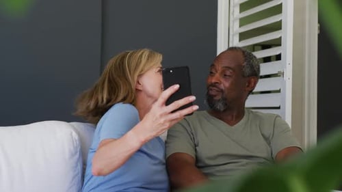 Smiling Couple Relaxing on Couch with Smartphone