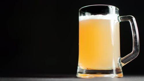 Cerveja leve dourada fresca com espuma branca fofa, rotação lenta, isolada no fundo preto do estúdio