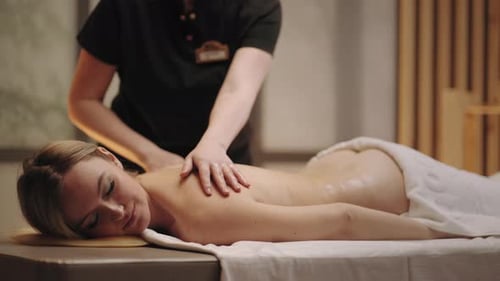 Charming Woman is Relaxing and Enjoying Massage in Spa Salon Professional Masseuse is Stroking Back
