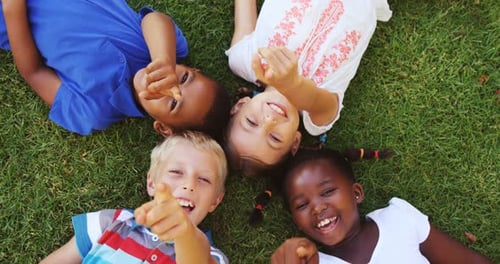 Joyful Children Lying on Grass Smiling and Pointing