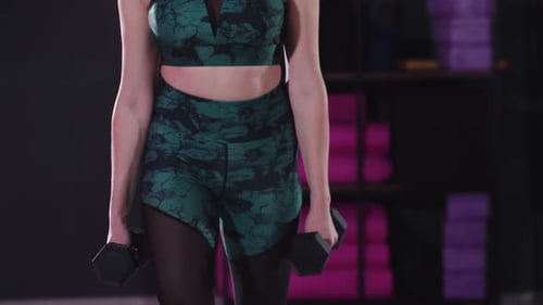 Young Sportive and Pretty Woman Doing Squats Holding Two Dumbbells in Fitness Hall