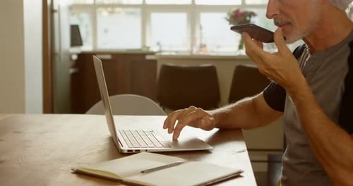 Älter Mann spricht auf dem Handy, während er Laptop benutzt 4k