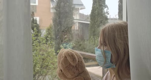 Side View of Adult Blond Caucasian Woman in Face Mask Holding Teddy Bear As Sitting on Windowsill