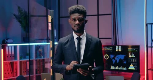 Homme d'affaires travaillant sur une tablette PC dans un bureau du soir, puis regardant la caméra avec un sourire sincère