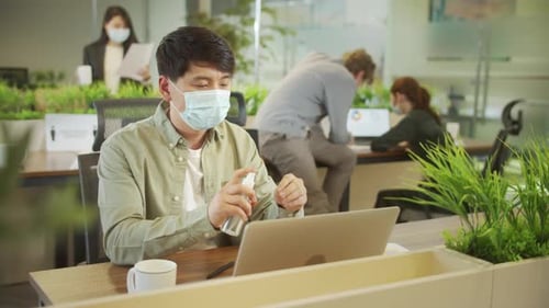 Man Applying Hand Sanitizer at Office with Mask