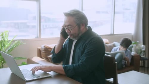 asian male dad using laptop and conversation on smartphone remotely distance working