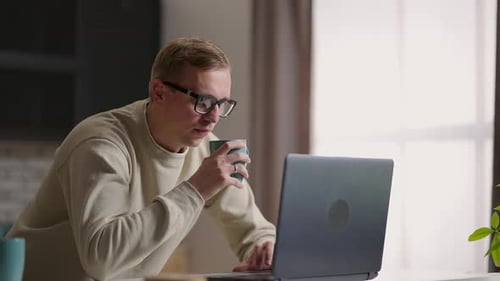 Man Working on Laptop Computer Drinking Coffee