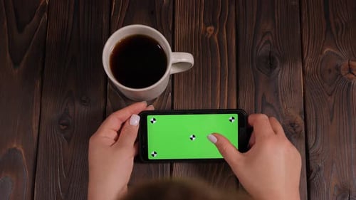 Nahaufnahme einer Frau, die Kaffee trinkt und ein Telefon mit grünem Bildschirm benutzt