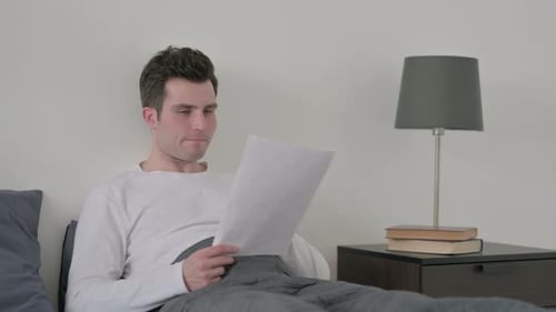 Man Reacting to Loss on Documents in Bed