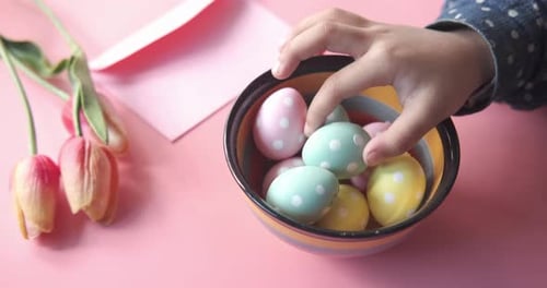 Child Reaches for Easter Egg in Colorful Bowl