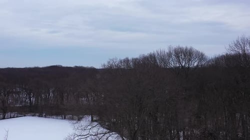 An aerial view from a drone, over a snow covered field during a cloudy sunrise. The camera boom up s