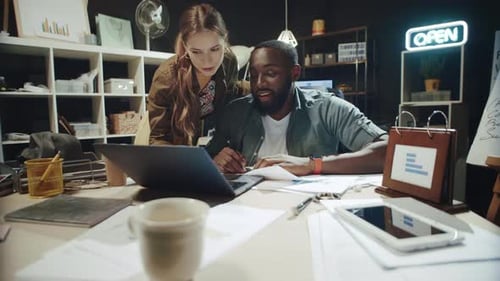 Female Professional Helping African American Man Worked at Laptop in Office.