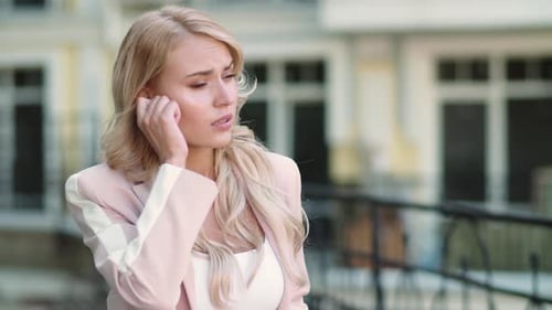 Blonde Woman Adjusting Earpiece Outdoors