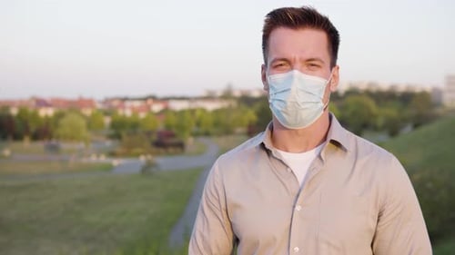 Ein junger kaukasischer Mann mit Gesichtsmaske spricht am Stadtrand mit der Kamera