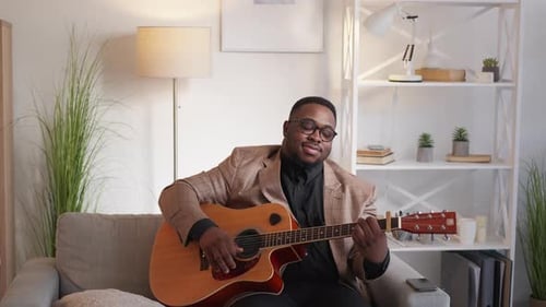 Man plays acoustic guitar on couch indoors