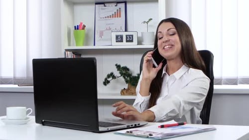 Business Woman Sitting in the Office in Front of a Laptop and Talking on the Phone
