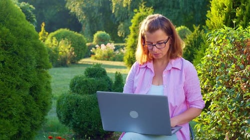 Young woman freelancer works remotely on a laptop on nature in the park.