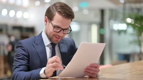 Happy Businessman Reading Documents at Office Workplace