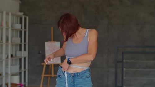 Woman Measuring Waist with Tape Measure in Home
