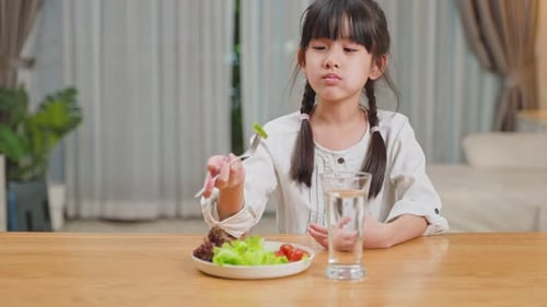 Asian young little girl child eat green vegetable salad in plate on dinner table for health.