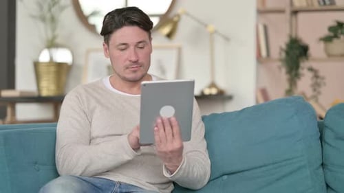 Man Sitting with Tablet on Sofa at Home