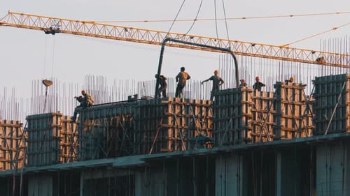 Building Construction. A Crane on a Construction Site Lifts a Load. Workers at a Construction Site