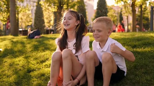 Portrait of a Happy Boy and Girl in the Park on the Grass at Sunset