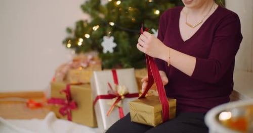 Woman Wraps Christmas Gift with Red Ribbon