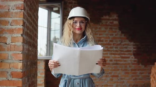 Eine junge Frau mit weißem Arbeitshelm, Jeanskleidung und Schutzbrille steht auf der Baustelle