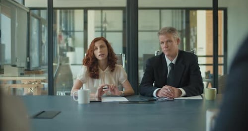 Two business people talk project strategy with their colleagues in the office meeting room.