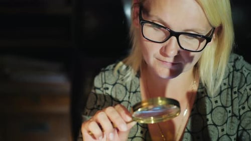 Eine Frau mit Brille betrachtet etwas durch eine Lupe. Sorgfältiges Studium