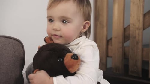 Infant Sits and Hugs Teddy Bear on Sofa