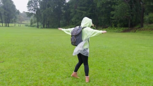 Woman in Poncho Twirling in Rainy Grassy Field