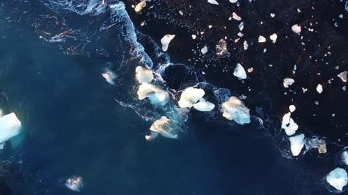 Olas de agua azul puro del océano con reflejos de luz aplastan los icebergs en la playa volcánica