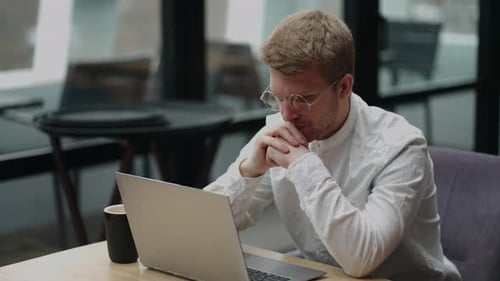 Smart Man with Glasses is Looking at Display of Laptop and Thinking Hard Concentrated Office Worker