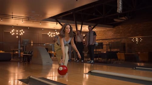 Eine Frau macht einen Wurf in einem Bowlingclub und genießt es, Pins emotional mit einem Ball auszuschlagen
