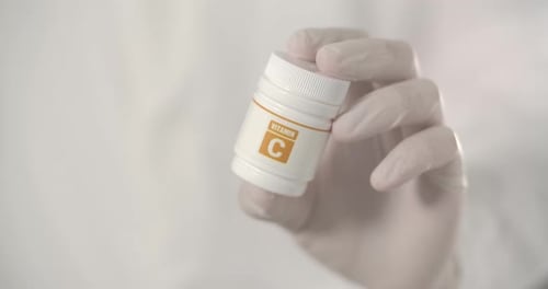 Gloved Hand Holds Vitamin C Bottle