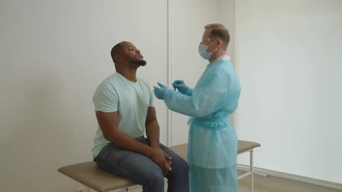 Male Physician in PPE Taking Black Patient Swab Sample for PCR Test for Coronavirus at Hospital