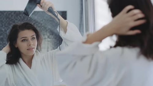 Woman in Robe Blow Drying Hair in Bathroom